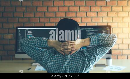 Asian programmers man are relaxing and looking at the code on the computer screen in the office. Stock Photo