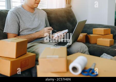Young asian man looking on computer laptop and writing order list on paper, SME concept. Stock Photo