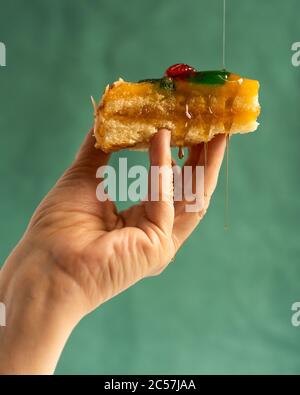 Vertical photo of a hand with a cake with caramelized fruit while they are adding liquid candy that gives away the cake with the green background Stock Photo