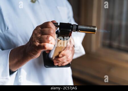 Detail of a cook's hands using a kitchen torch with the flame coming out Stock Photo