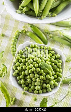 Green raw peas and pods in pocelain bow isolated on wooden table Stock Photo
