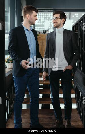 Two men walking down on wooden stairs chatting indoors. Communication concept Stock Photo