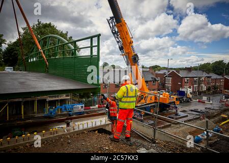 A57 Hyde Road in Gorton has a new footbridge added to the old railway line now Fallowfield cycle loop part of the road widening with Ainscough crane Stock Photo