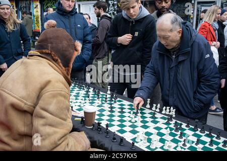 Elderly Chinese man playing chess on Brick Lane on market day on 2nd February 2020 in London, England, United Kingdom. Brick Lane Market is a London Sunday market centred on Brick Lane, in Tower Hamlets in east London. It is located at the northern end of Brick Lane and in the heart of east Londons Bangladeshi community.