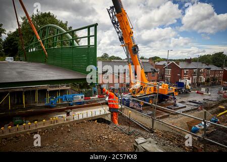 A57 Hyde Road in Gorton has a new footbridge added to the old railway line now Fallowfield cycle loop part of the road widening with Ainscough crane Stock Photo