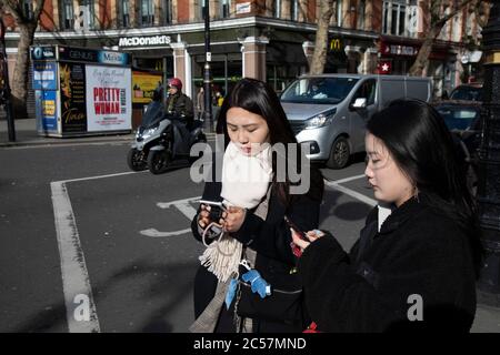 Two Chinese woman checking their smart phones on 18th February 2020 in London, England, United Kingdom. Stock Photo