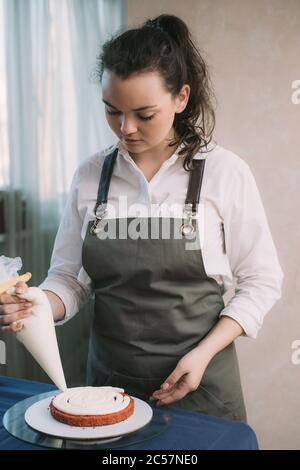 The hands of a bakers girl squeeze pink cream onto a cake base. Stock Photo
