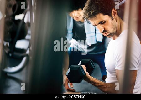 Muscular man working out in gym doing exercises with dumbbells at biceps Stock Photo