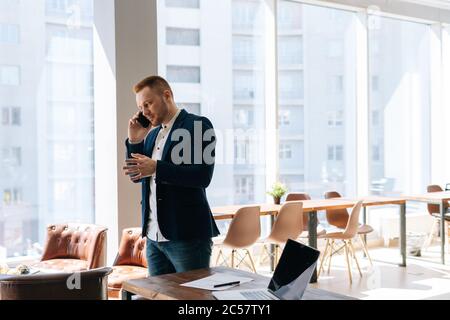 Handsome young businessman wearing fashion suit is talking on mobile phone in modern office room Stock Photo