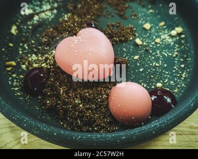 A close-up photo of a fragment of a turquoise plate with a pink dessert in the form of a heart and a round ball in biscuit crumb. Focus in the center Stock Photo