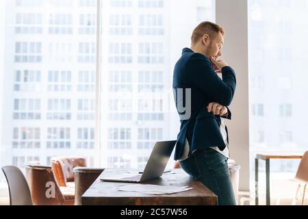 Side view of thoughtful young business man wearing suit clothing is standing in modern office room Stock Photo