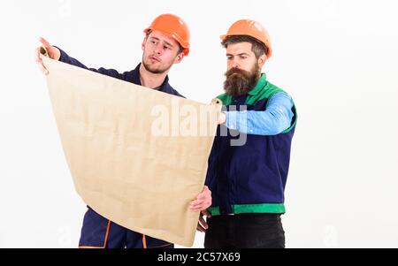 Men in helmets with blueprint on white background. Architect and build concept. Architects in hard hat on strict face looks at drawing, plan, project. Builder, engineer, architect work at site. Stock Photo
