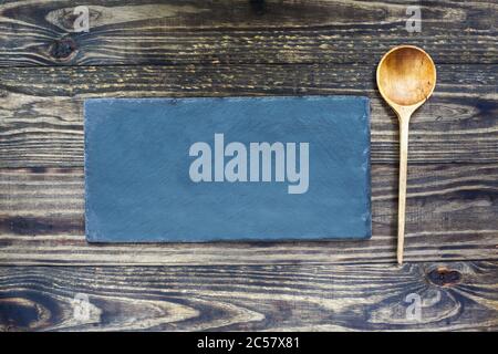 Old handcrafted wooden spoon with deep bowl made of olive wood lying near a slate stone over a rustic wood table background. Image shot from top view. Stock Photo