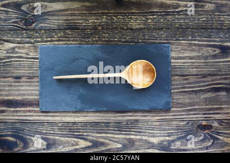 Old handcrafted wooden spoon with deep bowl made of olive wood over a slate stone and rustic wood table background. Image shot from top view. Flatlay. Stock Photo