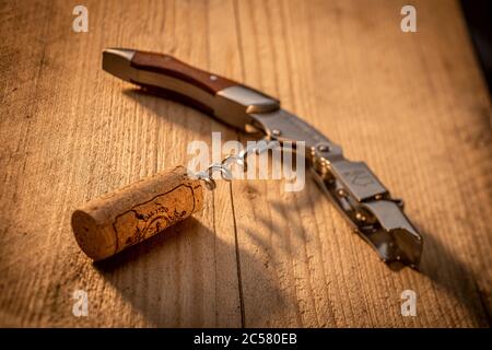 Corkscrew on sunlit wooden table with cork Stock Photo
