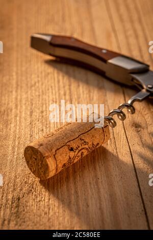 Corkscrew on sunlit wooden table with cork Stock Photo