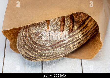 Freshly baked sourdough loaf of bread in brown paper bag on whitewashed boards Stock Photo