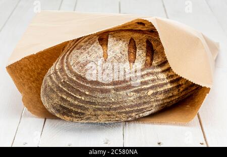 Freshly baked sourdough loaf of bread in brown paper bag on whitewashed boards Stock Photo