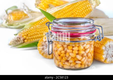 A glass jar filled with sweet canned corn. Fresh and cooked corn on cobs. Close up, side view, high-resolution product image. Stock Photo