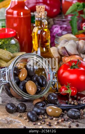 Black and green olives with olive oil and vegetables on a rustic wooden background. Close up, side view, high-resolution product image. Stock Photo