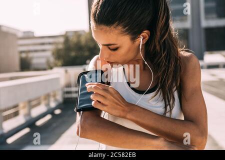 Woman listening to music with earphones from her smart phone while exercising in the city. Female in sportswear using a smartphone to monitor her prog Stock Photo