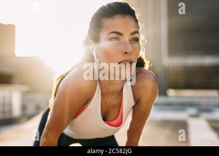 Female runner standing bent over and catching her breath after a running session in city. Sports woman taking break after a run. Stock Photo