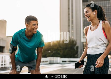 Two people taking a break after training session outdoors and smiling. Man and woman relaxing after a workout and laughing in the city. Stock Photo