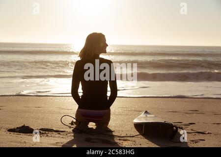 Woman with surfboard sitting on the beach Stock Photo