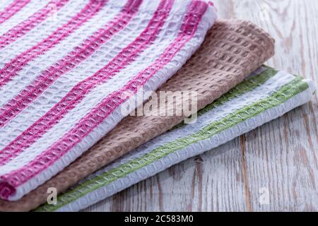 A stack of towels and napkins lying on the table. Clean kitchen towels, hand wipes lying on the table. Order in the kitchen. Colored napkins, towels. Stock Photo