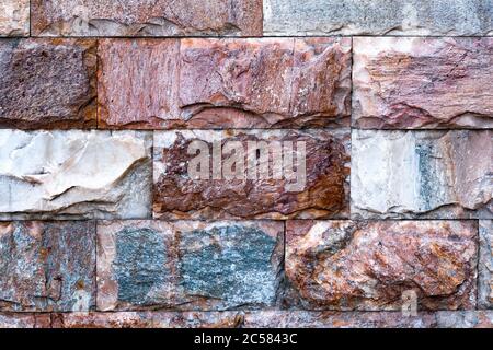 The wall is made of textured marble of different colors. A stone wall with an interesting marble texture. The marble facing of the wall. Stock Photo