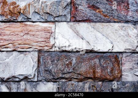 The wall is made of textured marble of different colors. A stone wall with an interesting marble texture. The marble facing of the wall. Stock Photo
