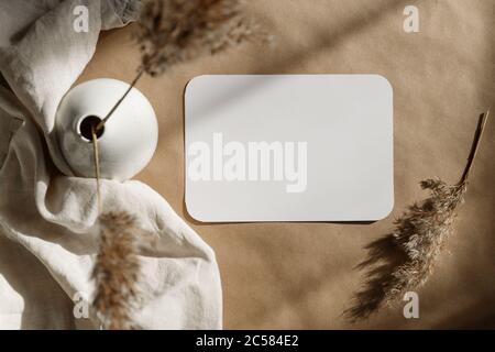 Blank paper sheet on a kraft paper with a ceramic vase and dry grass. Minimalist toned background. Stock Photo