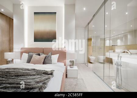 Luxury master bedroom with double bed next to elegant bathroom behind glass wall Stock Photo