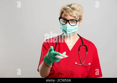 Portrait of female doctor wearing face mask handing tablets on grey background with copy space advertising area Stock Photo