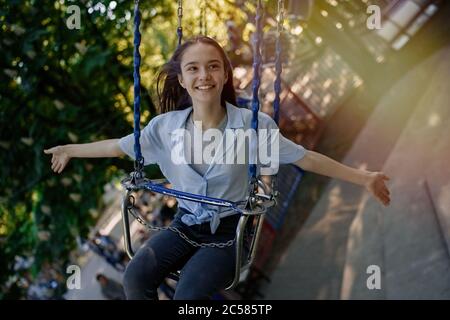 Happy child teenage girl riding chain carousel swing at amusement park Stock Photo