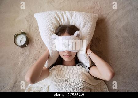 Sleepy teenager girl turning alarm off in the morning while lying in bed Stock Photo
