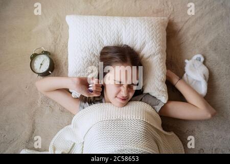 Sleepy teenager girl turning alarm off in the morning while lying in bed Stock Photo