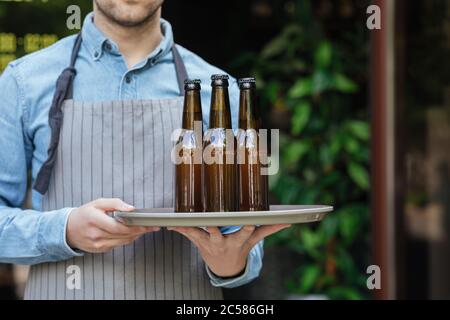 Barman in apron carries tray with bottles of beer in bar Stock Photo