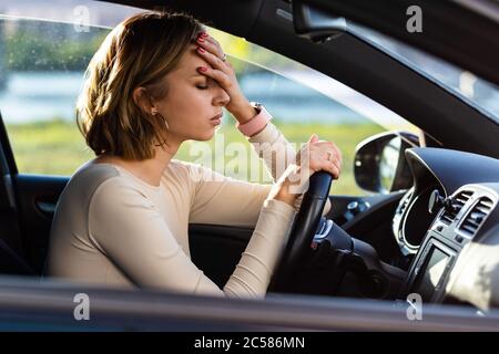 Exhausted woman driver feeling headache, sitting inside her car, keeping hand to head and feeling anxiety. Stop after driving car in traffic jam.Blood Stock Photo