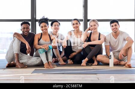 Portrait Of Smiling Multiethnic People Posing On Mats After Yoga In Studio Stock Photo