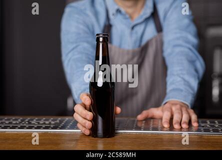 Evening in pub. Bartender gives to client bottle of beer at bar Stock Photo