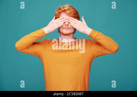 Calm young redhead man with beard closing eyes with hands in anticipation of surprise Stock Photo