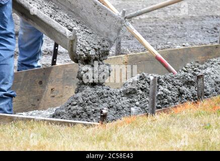 Workers pour cement into mold of a new sidewalk.  Photo shows motion of moving cement or concrete Stock Photo
