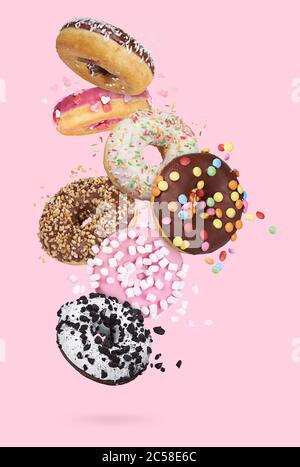flying glazed round doughnuts. Mix of multicolored sweet donuts with sprinkles on pink background Stock Photo