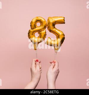 Female hand holding a number 85 birthday anniversary celebration gold balloon Stock Photo