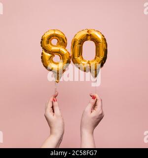 Female hand holding a number 80 birthday anniversary celebration gold balloon Stock Photo
