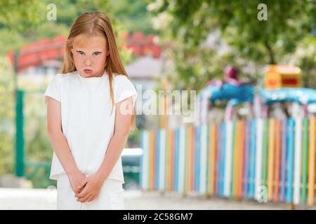 Emotions and facial expressions. Portrait of a distressed little girl, pouting. In the background is a kindergarten. Outdoor. Stock Photo