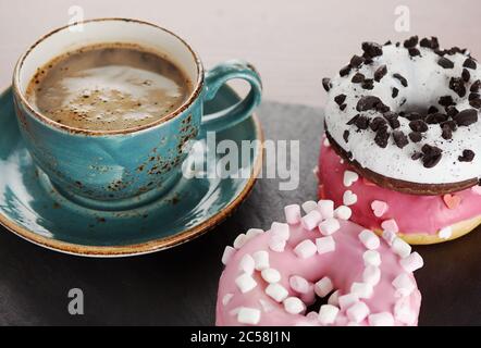 Cup of coffee and glazed doughnuts with sprinkles on kitchen table Stock Photo