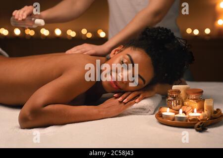 Therapist applying massage oil on beautiful black lady body Stock Photo