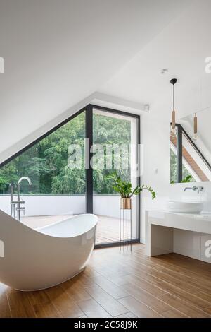 Elegant attic bathroom with big bathtub, wooden floor and balcony window Stock Photo